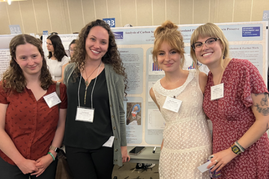 Four students standing in front of poster in research colloquium