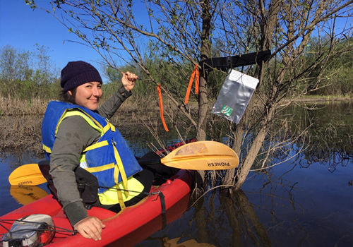 Student in kayak in a wetland with audio recorder in view