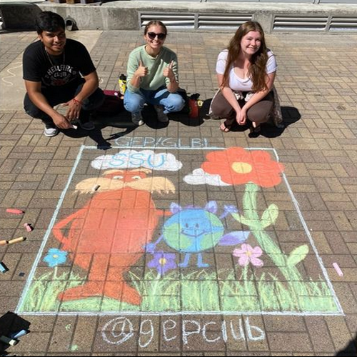 Three students posed in front of chalk picture of lorax