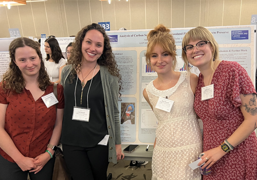 Four students standing in front of poster in research colloquium