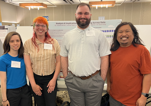 Three students and Dr. Fang standing in front of poster in research colloquium